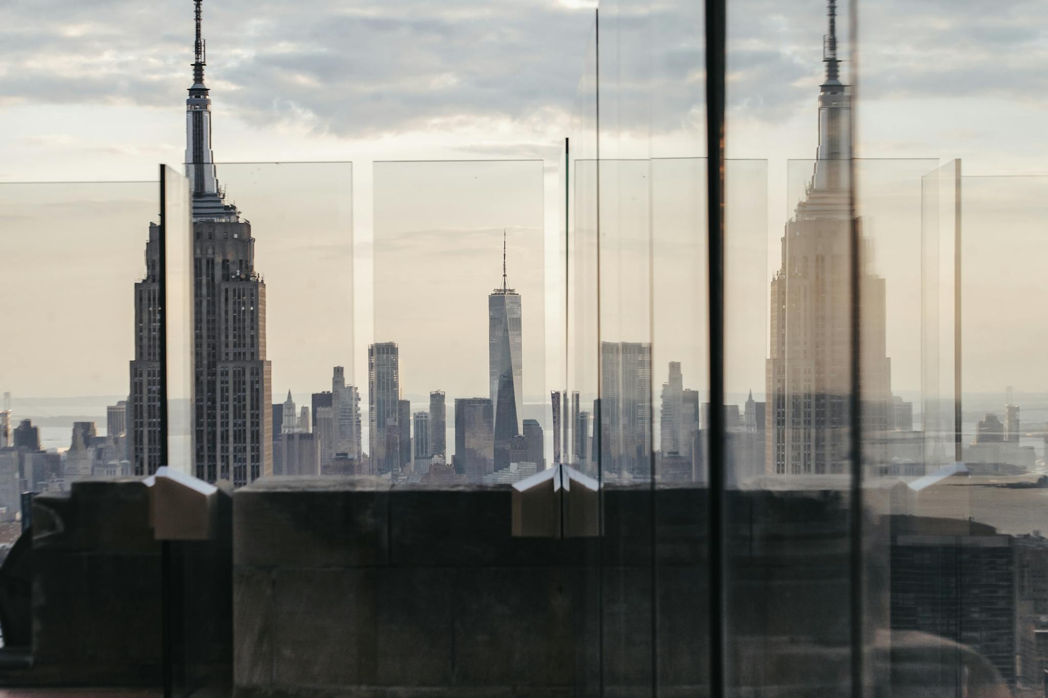 Through fenced rooftop view of skyscraper facade under cloudy sky in New York City